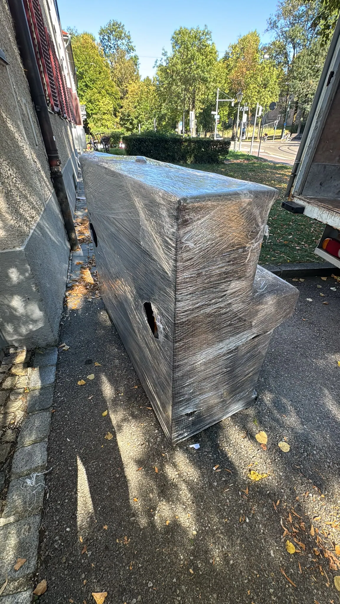 Mit Schutzfolie verpacktes aufrechtes Klavier neben einem Transportfahrzeug